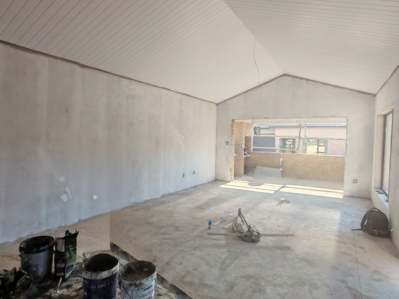 An unfinished living room space featuring a vaulted ceiling, exposed brickwork, and concrete flooring, currently undergoing renovation.