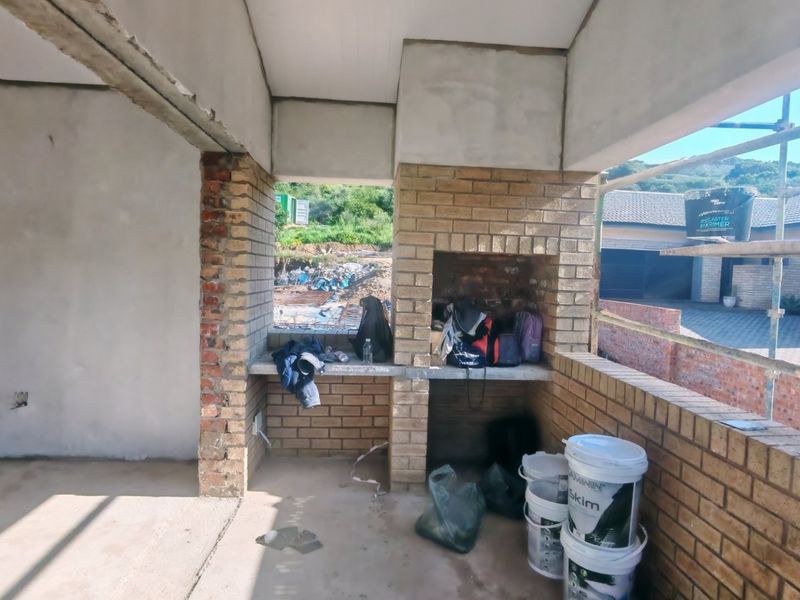 An unfinished outdoor patio area featuring a built-in brick braai and concrete counter, currently under construction with exposed brick and structural elements.