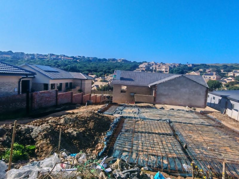 A construction site showing a prepared concrete foundation with steel reinforcement mesh, surrounded by neighboring residential properties.