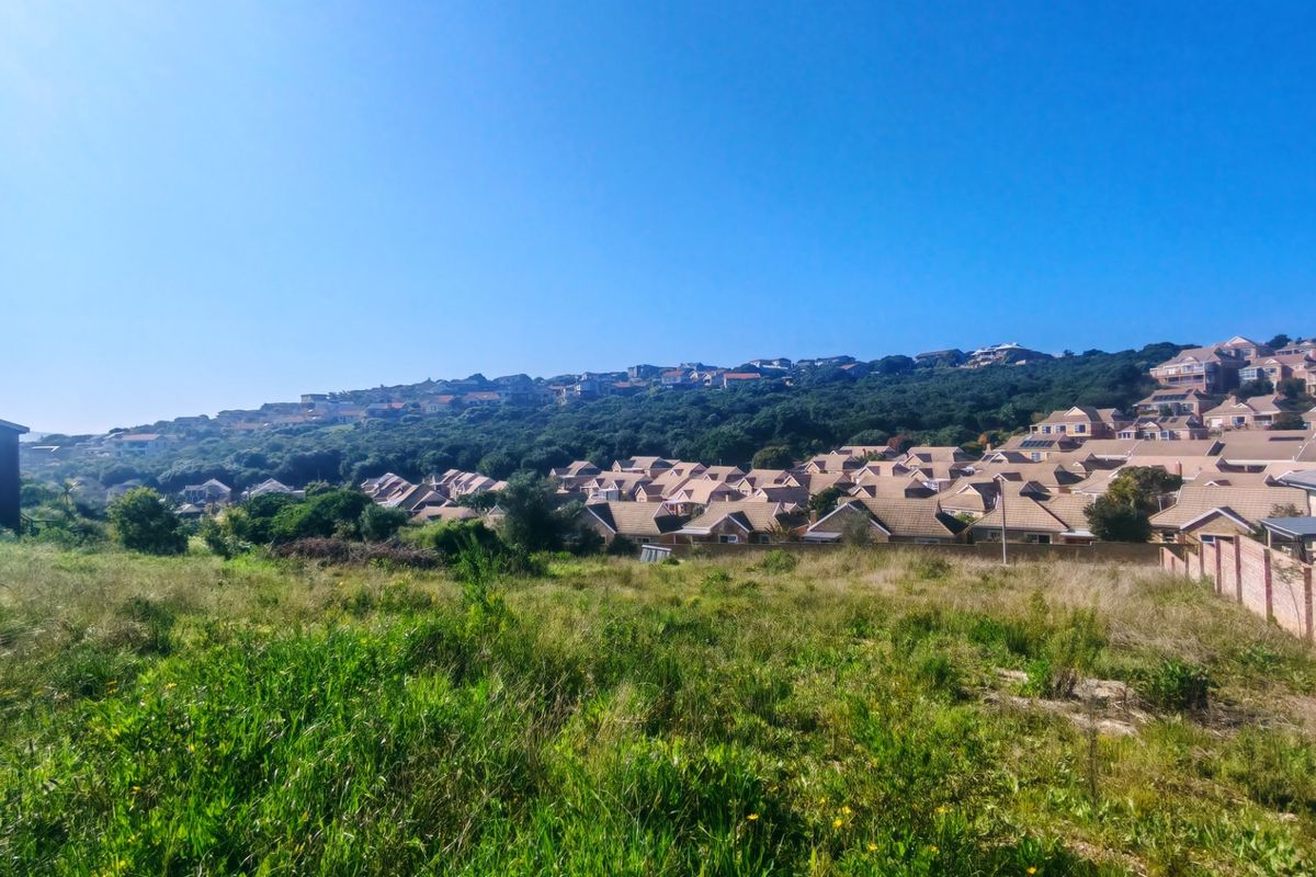 A wide-angle view of a vacant residential plot overlooking a developed suburban neighborhood with established housing and natural vegetation.
