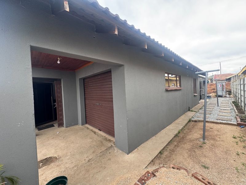 Rear exterior view showing a garage with a roller shutter door, concrete patio area, and a paved walkway leading along the side of the house.