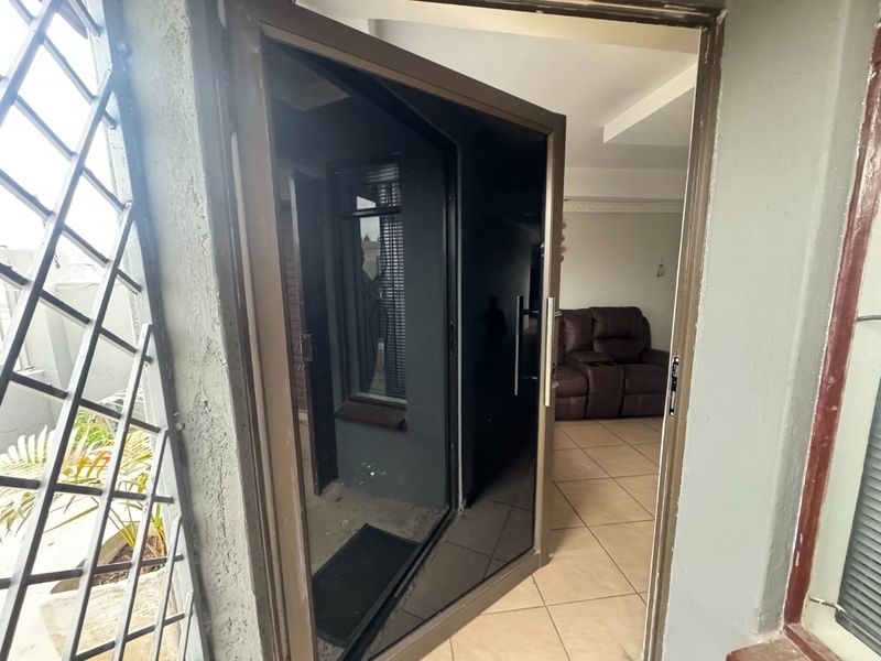 Entrance area featuring a modern dark-tinted aluminium glass door and tiled flooring, providing a clear view into the adjacent living space.