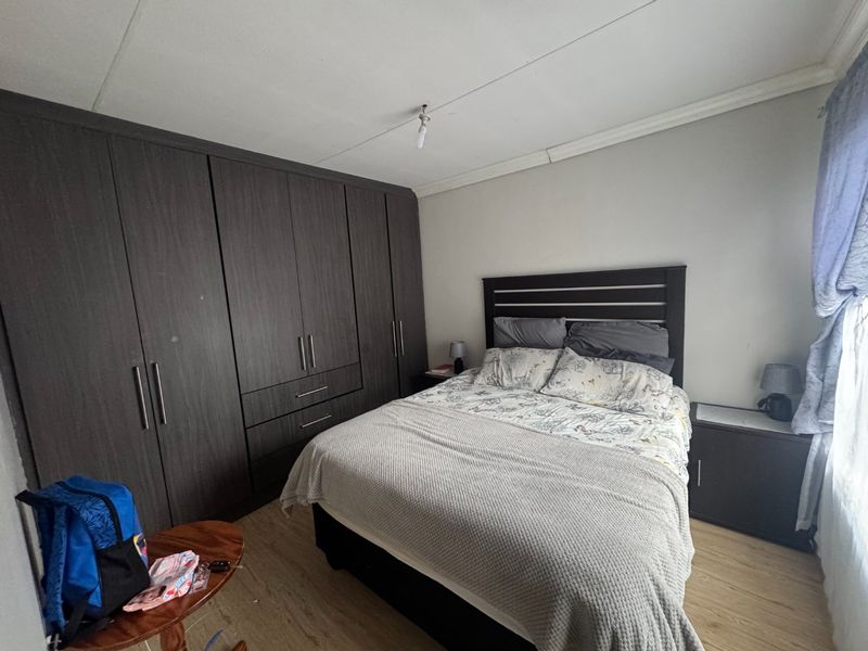 A bedroom featuring dark wood built-in cupboards, laminate flooring, and a coved ceiling, providing functional storage and a neutral base.
