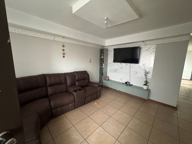 A living room featuring tiled flooring, a built-in media console with a marble-effect feature wall, and decorative ceiling cornicing.