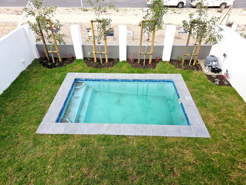 A compact, well-maintained swimming pool set within a landscaped garden, featuring a paved surround and integrated pool filtration system.