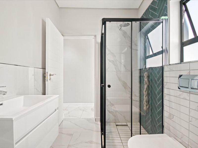 Modern bathroom featuring a walk-in shower with black frame, herringbone accent tiling, wall-mounted toilet, and a sleek vanity unit with marble-effect flooring.