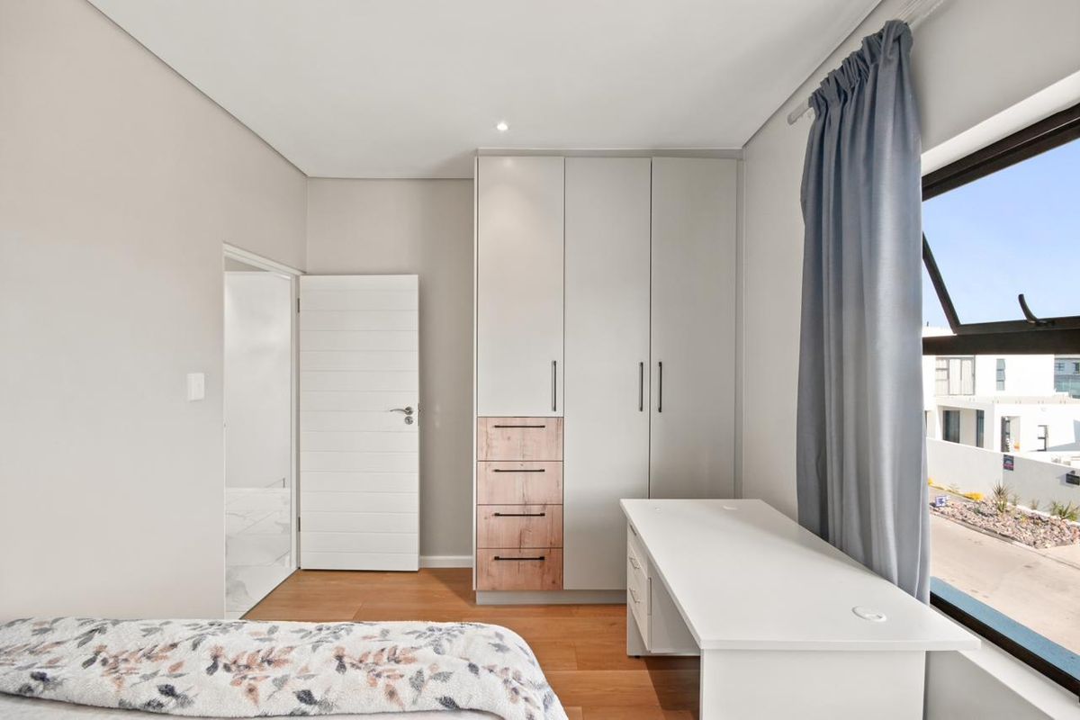 A modern bedroom featuring built-in cupboards with wood-accented drawers, laminate flooring, and a large window providing natural light.