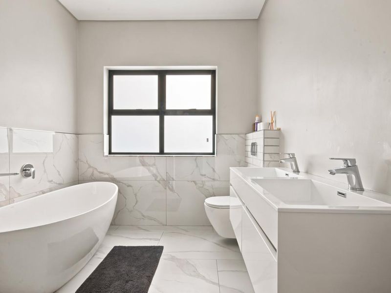 Modern bathroom featuring a sleek freestanding bathtub, wall-mounted toilet, and a contemporary double vanity with marble-look tiling throughout.
