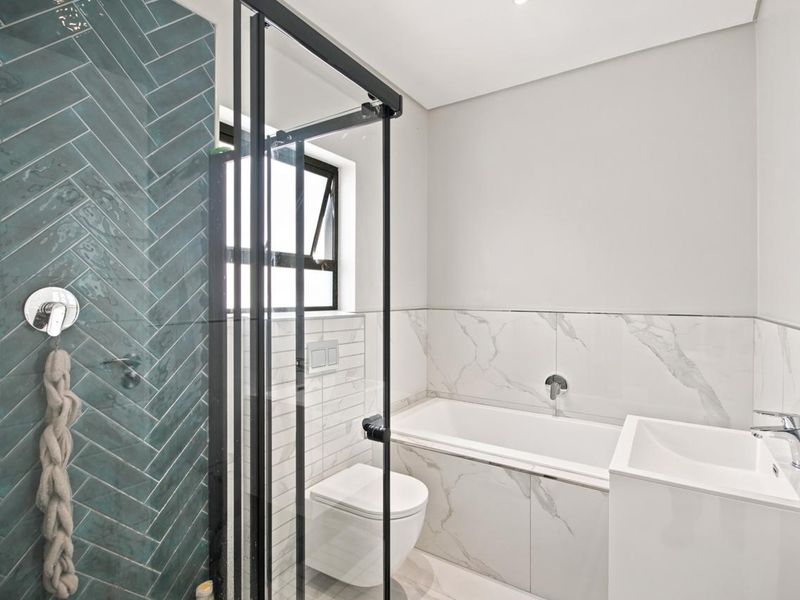 Modern bathroom featuring a glass-enclosed shower with teal herringbone tiles, a built-in bathtub, and a wall-mounted toilet with marble-look finishes.