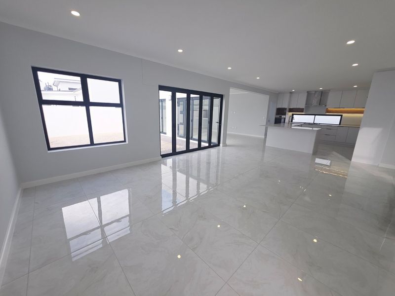 Spacious open-plan living area featuring polished porcelain tiles, modern kitchen with island, and large aluminium stacker doors leading to the exterior.