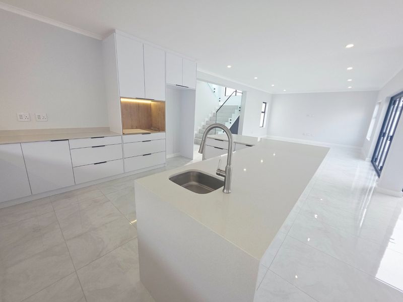 Modern open-plan kitchen featuring a central island with quartz countertops, sleek white cabinetry, and polished tiled flooring, seamlessly flowing into the living area.