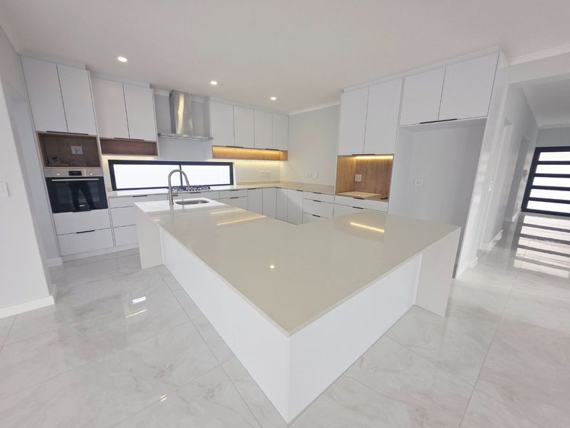 Modern, high-end kitchen featuring sleek white cabinetry, quartz countertops, integrated appliances, and polished porcelain floor tiles in a bright, open-plan layout.
