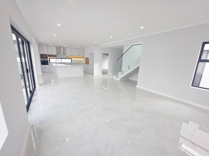 Spacious open-plan living area featuring a modern kitchen with island, sleek tiled flooring, and a contemporary staircase with glass balustrade.