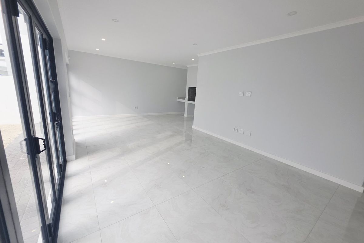 A bright, spacious, and empty living area featuring modern marble-look floor tiles, recessed lighting, and large sliding glass doors leading to the exterior.