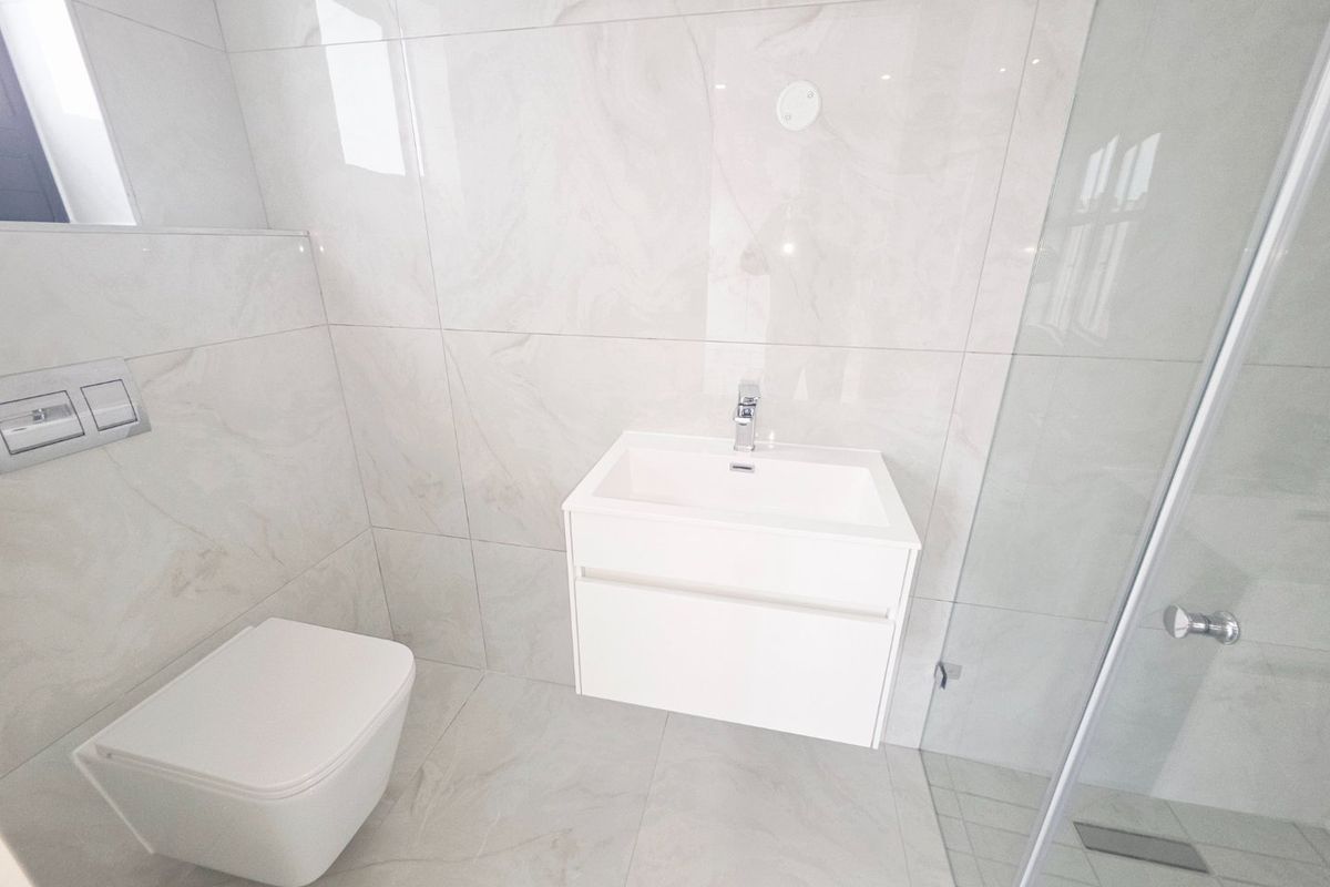 Modern bathroom featuring a wall-mounted toilet with concealed cistern, a sleek vanity unit with basin, and a glass-enclosed shower with neutral marble-look tiling.