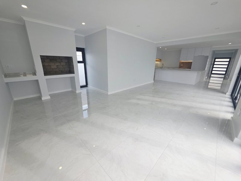 Spacious open-plan living area featuring polished tile floors, a built-in fireplace, and a modern kitchen with sleek cabinetry and stone countertops.