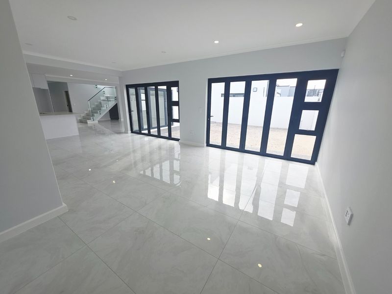 Spacious open-plan living area featuring polished porcelain tiles, modern recessed lighting, and large aluminium stacker doors leading to the exterior.
