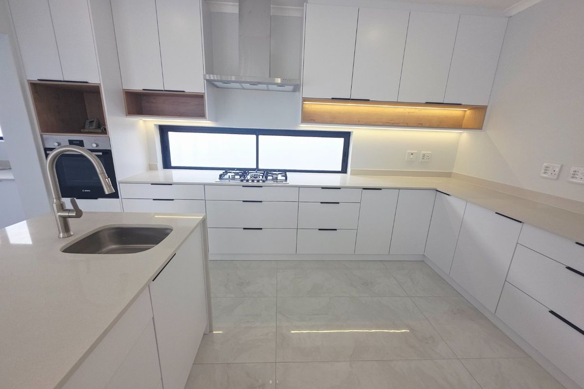 Modern, well-appointed kitchen featuring sleek white cabinetry, quartz countertops, integrated appliances, and high-quality porcelain floor tiles with ambient under-cabinet lighting.