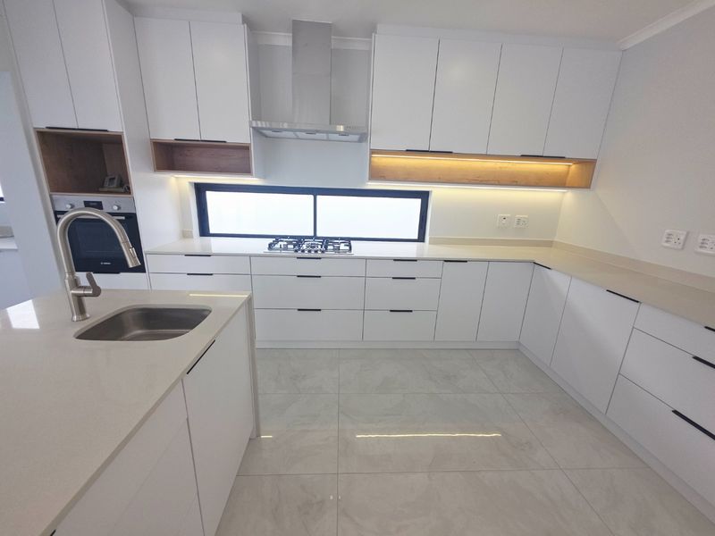 Modern, well-appointed kitchen featuring sleek white cabinetry, quartz countertops, integrated appliances, and high-quality porcelain floor tiles with ambient under-cabinet lighting.