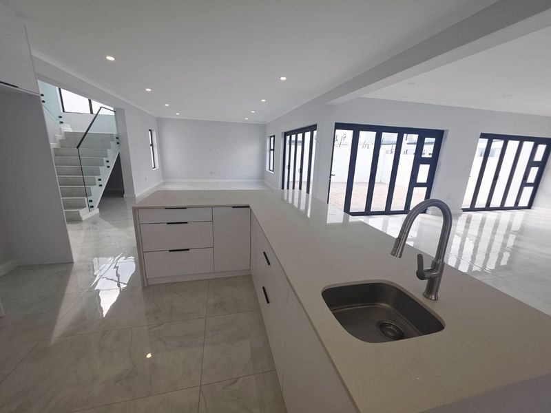 Modern open-plan kitchen and living area featuring a central island, sleek cabinetry, high-gloss floor tiles, and seamless access to the outdoor space via bi-fold doors.