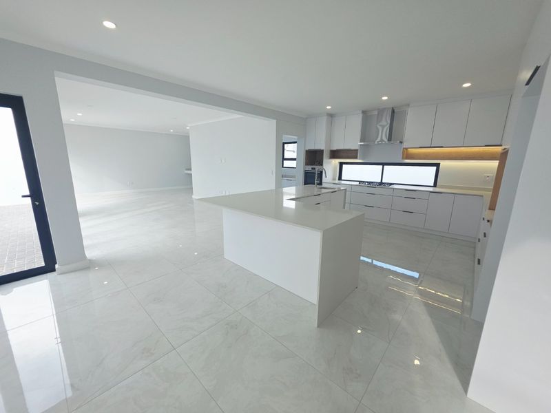 Modern open-plan kitchen featuring a central island, sleek white cabinetry, integrated appliances, and polished porcelain floor tiles in a bright, spacious layout.