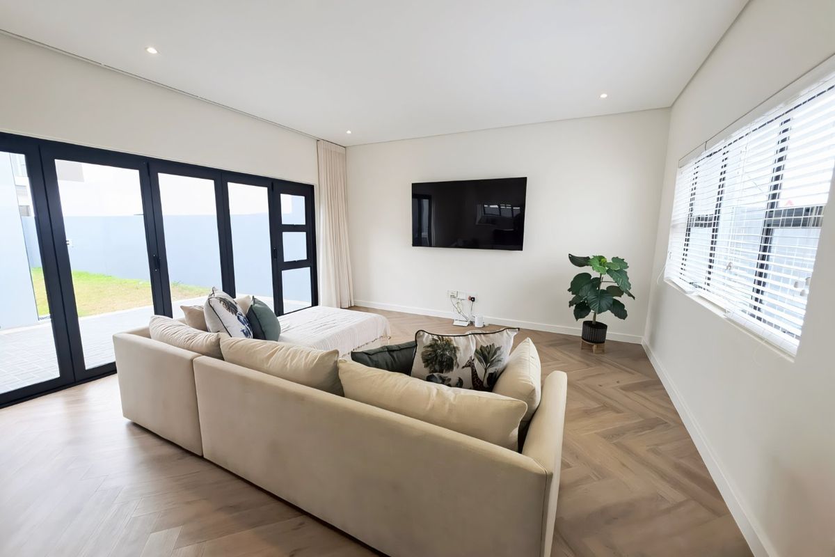 Modern living room featuring elegant herringbone timber flooring, recessed downlighting, and large black aluminium stacker doors providing seamless access to the outdoor area.