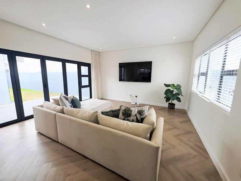 Modern living room featuring elegant herringbone timber flooring, recessed downlighting, and large black aluminium stacker doors providing seamless access to the outdoor area.