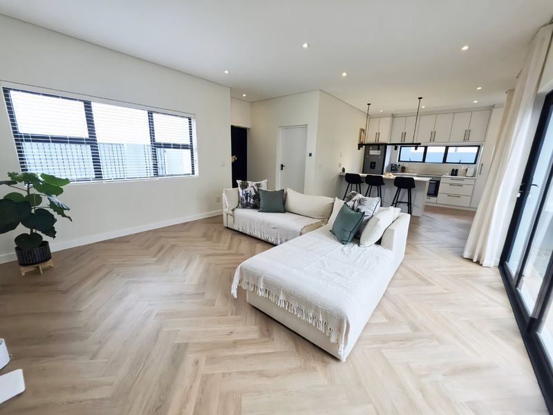 Modern open-plan living area featuring light herringbone timber flooring, recessed lighting, and a sleek kitchen with a central island and built-in cabinetry.