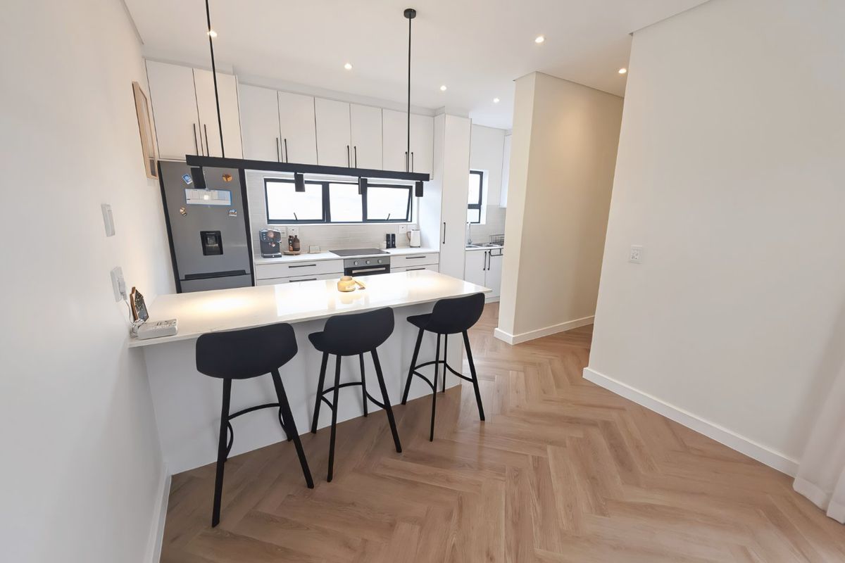 Modern kitchen featuring a central island with breakfast bar seating, sleek white cabinetry, herringbone flooring, and integrated appliances.