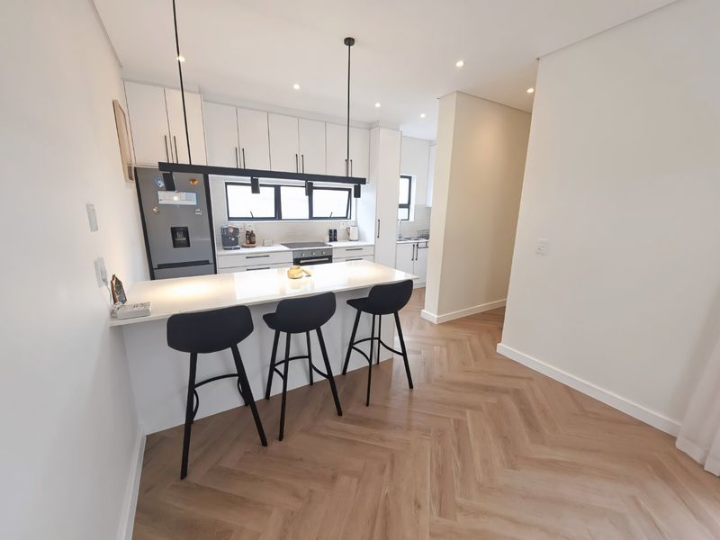 Modern kitchen featuring a central island with breakfast bar seating, sleek white cabinetry, herringbone flooring, and integrated appliances.