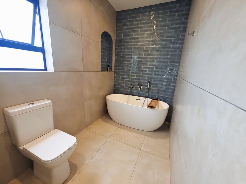 Modern bathroom featuring a sleek freestanding bathtub, wall-mounted fixtures, a recessed niche, and contemporary large-format wall tiles.