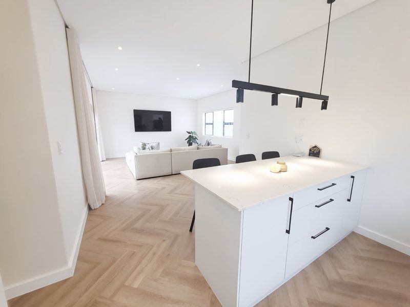 Modern open-plan living area featuring a central kitchen island with stone countertops, herringbone timber flooring, and contemporary pendant lighting.