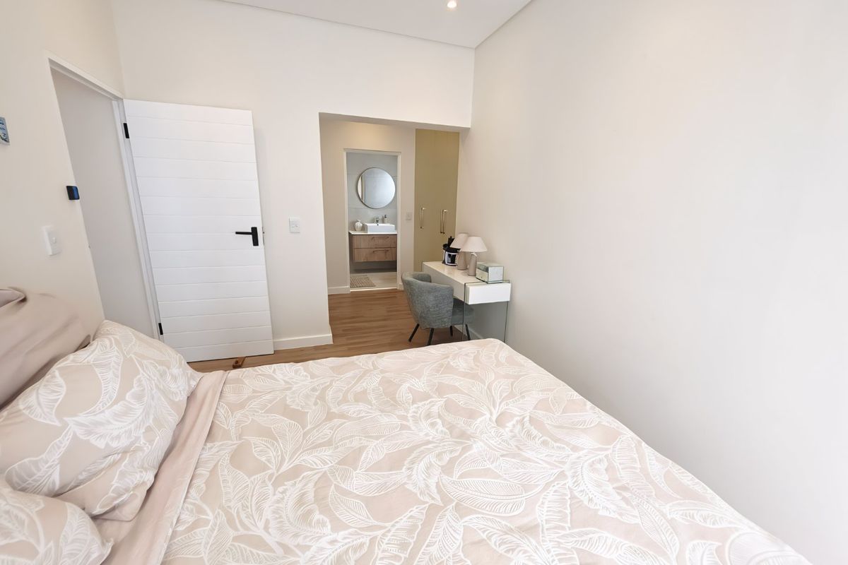 A bright, modern bedroom featuring laminate flooring, built-in cupboards, and an adjoining en-suite bathroom with contemporary finishes.