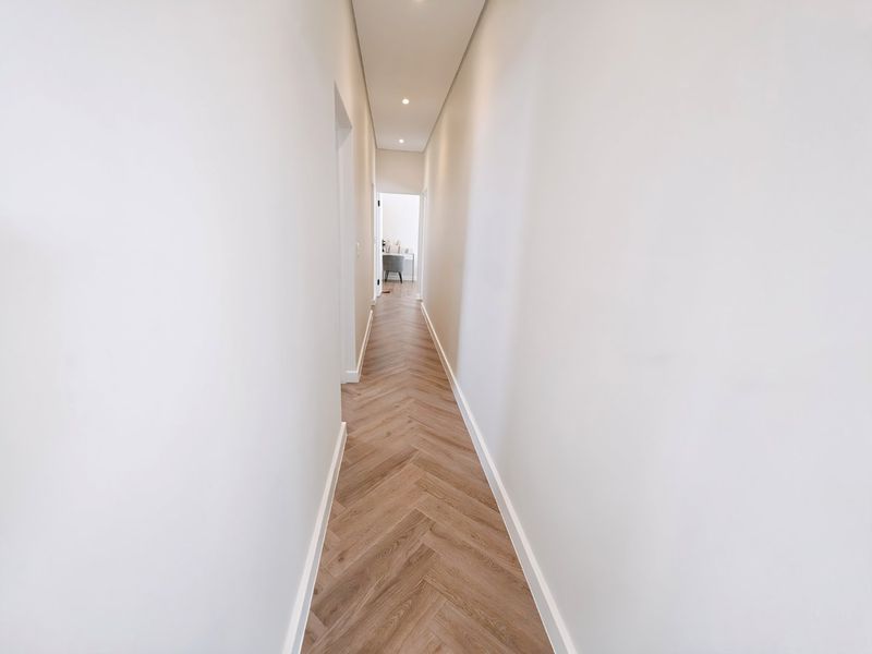 A bright, modern hallway featuring high-quality herringbone wood flooring and clean, minimalist white walls with recessed ceiling lighting.