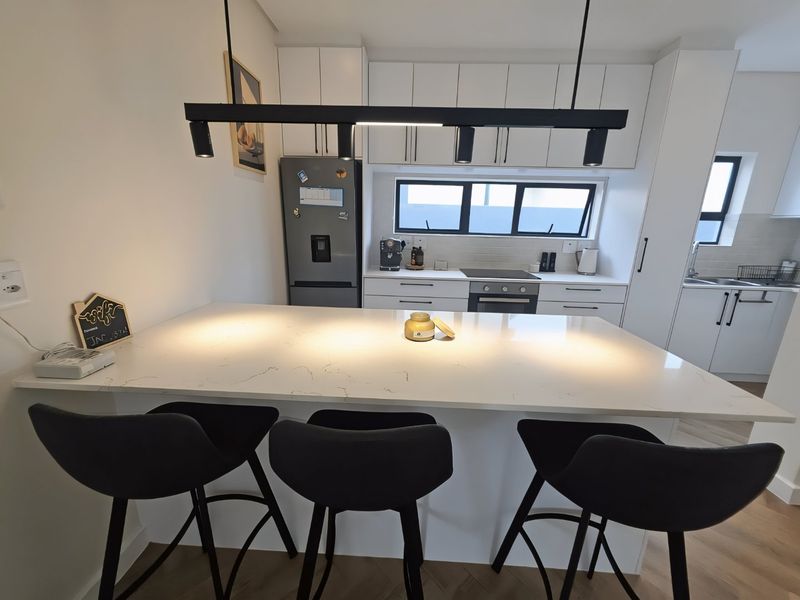 Modern kitchen featuring white cabinetry, quartz countertops, a breakfast island with pendant lighting, and integrated appliances.