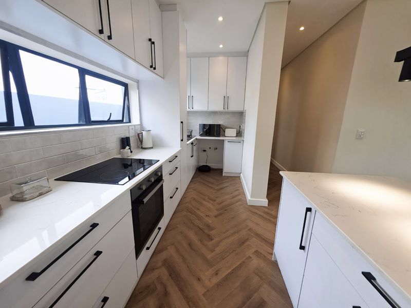 Modern galley kitchen featuring white cabinetry, stone countertops, herringbone flooring, and integrated appliances including an induction cooktop and built-in oven.
