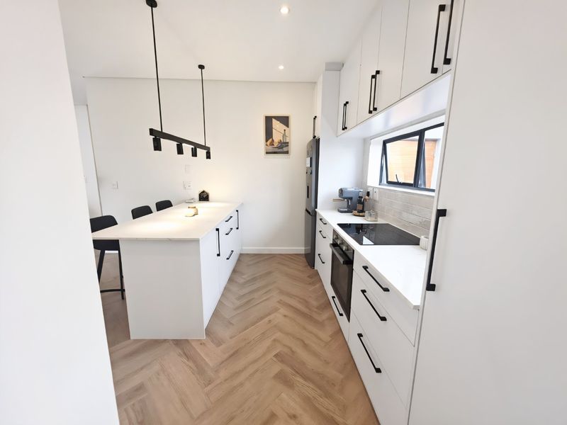Modern kitchen featuring a central island, herringbone timber flooring, sleek white cabinetry with black hardware, and integrated appliances.