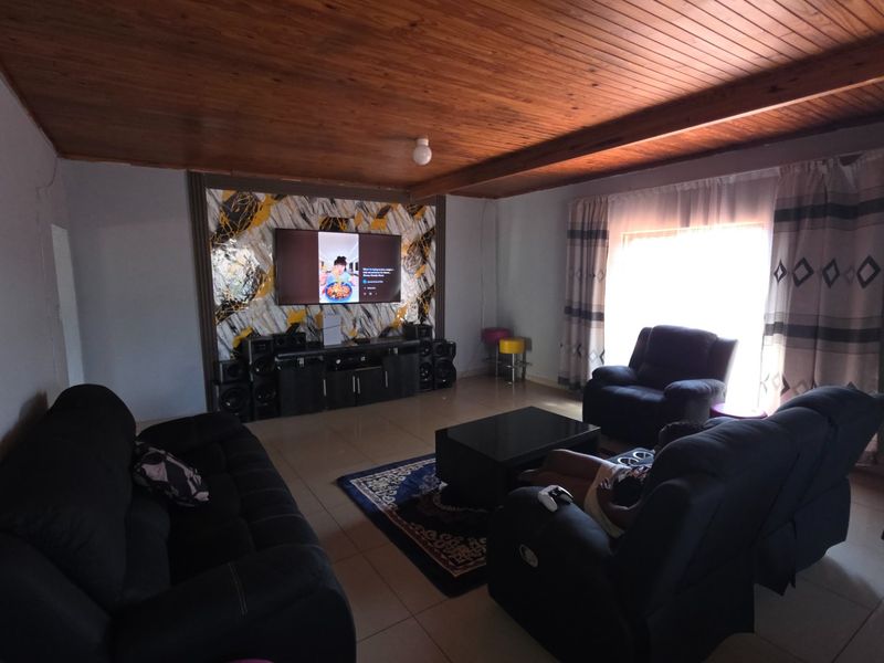 Spacious living room featuring a warm timber-clad ceiling, tiled flooring, and a decorative feature wall, offering a comfortable and inviting atmosphere.