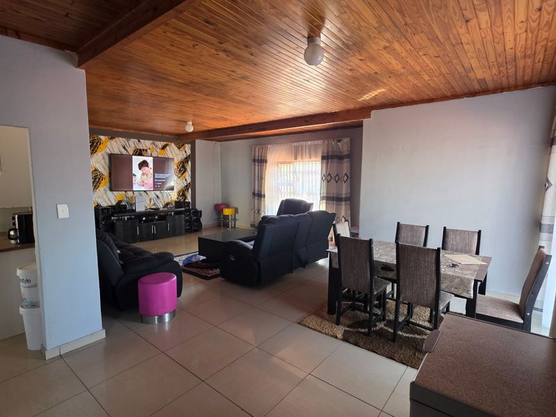 Spacious open-plan living and dining area featuring a warm timber-clad ceiling, neutral tiled flooring, and an adjacent kitchen space.