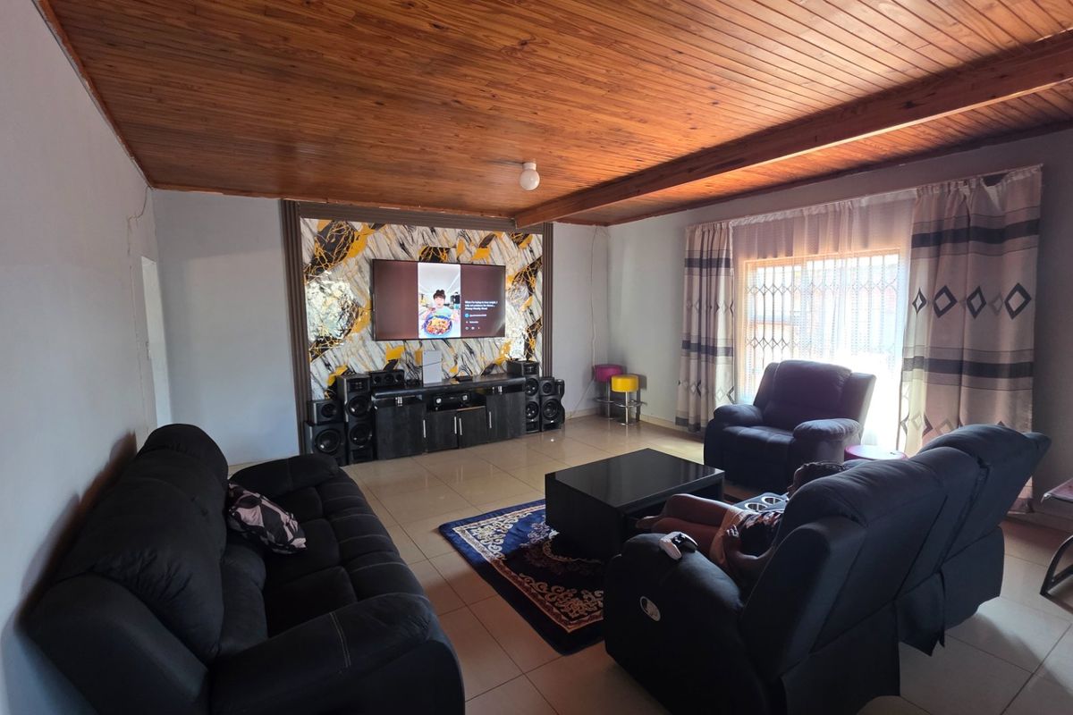Spacious living room featuring a warm timber tongue and groove ceiling, tiled flooring, and a decorative feature wall.