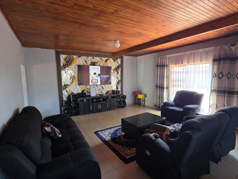 Spacious living room featuring a warm timber tongue and groove ceiling, tiled flooring, and a decorative feature wall.