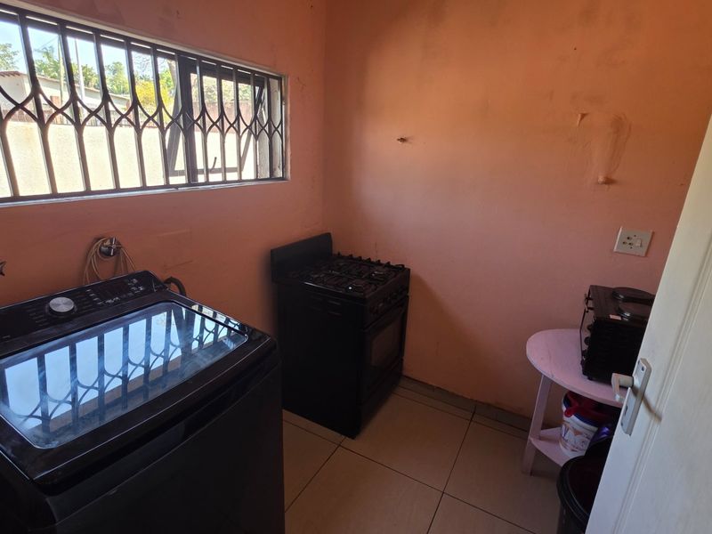 A compact kitchen area featuring tiled flooring, a gas stove, and security bars on the window, requiring cosmetic updates to the wall finishes.
