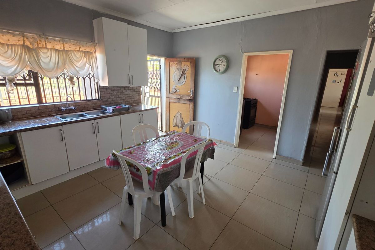 A functional kitchen featuring tiled flooring, built-in cabinetry, and a tiled backsplash, with direct access to an adjacent room and exterior door.