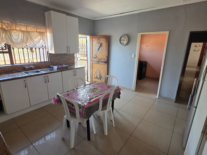 A functional kitchen featuring tiled flooring, built-in cabinetry, and a tiled backsplash, with direct access to an adjacent room and exterior door.