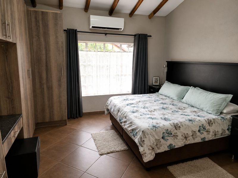 A well-maintained bedroom featuring exposed timber ceiling beams, built-in cabinetry, tiled flooring, and a wall-mounted split-system air conditioner.