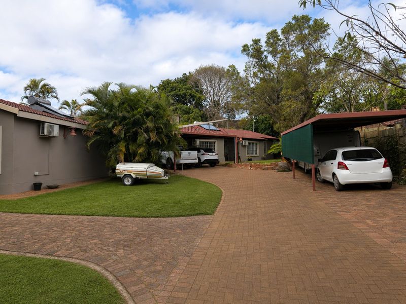 Front exterior view of the property featuring a paved driveway, carport, and well-maintained garden area with established trees.