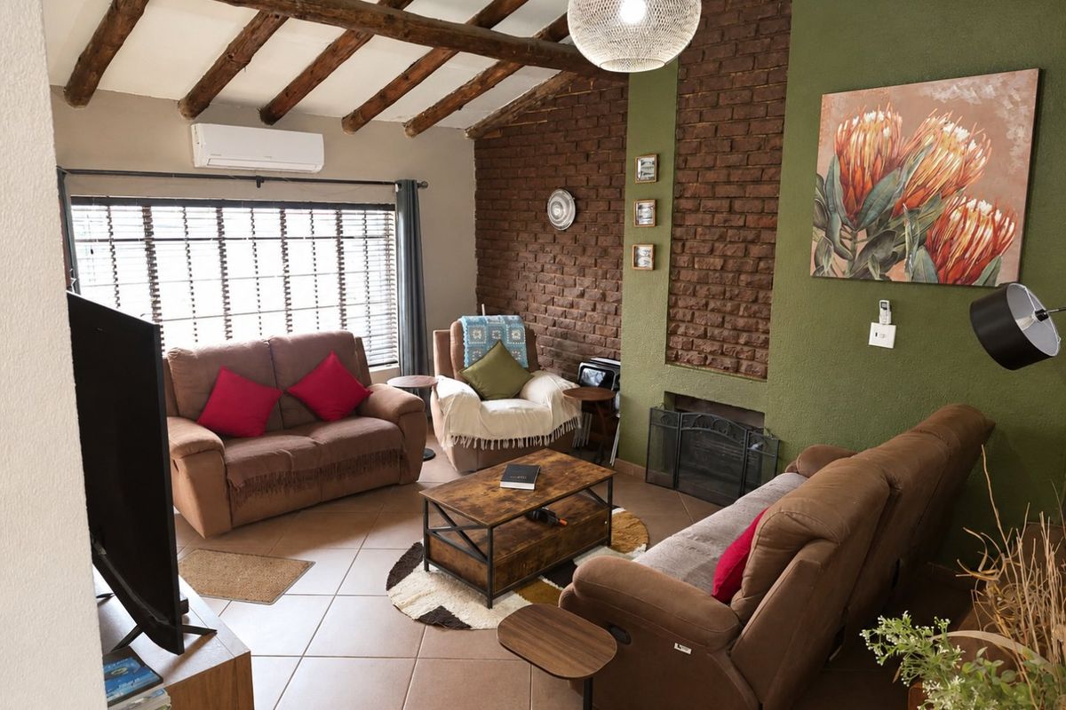 Cozy living room featuring a rustic brick fireplace, exposed timber ceiling beams, and tiled flooring, complemented by a wall-mounted air conditioning unit.