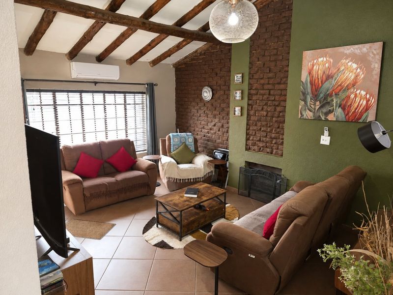 Cozy living room featuring a rustic brick fireplace, exposed timber ceiling beams, and tiled flooring, complemented by a wall-mounted air conditioning unit.