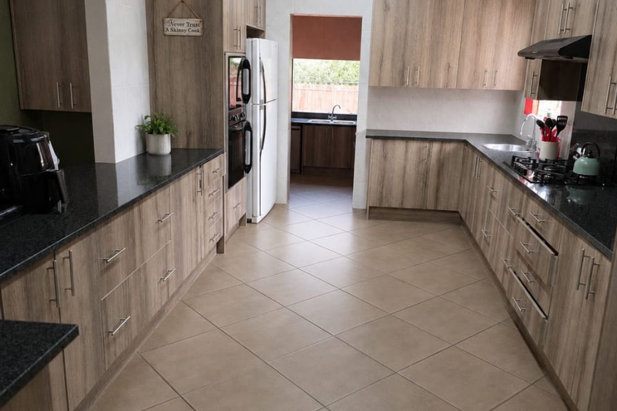 Spacious kitchen featuring modern wood-look cabinetry, granite countertops, built-in double oven, gas hob, and exposed timber rafters with tiled flooring throughout.