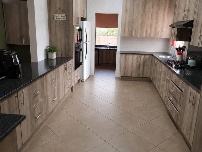 Spacious kitchen featuring modern wood-look cabinetry, granite countertops, built-in double oven, gas hob, and exposed timber rafters with tiled flooring throughout.